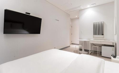 a white room with a bed and a desk and a television at H Avenue Hotel Idae Shinchon in Seoul