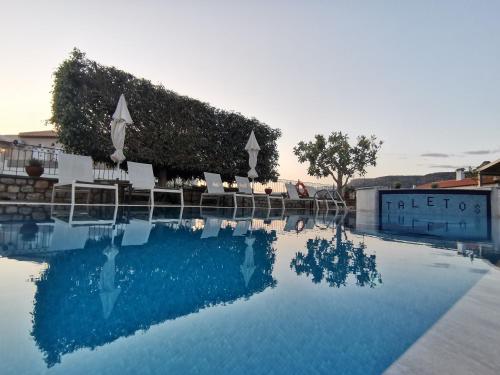 a swimming pool with chairs and the reflection in the water at Taletos Apartments in Stoupa