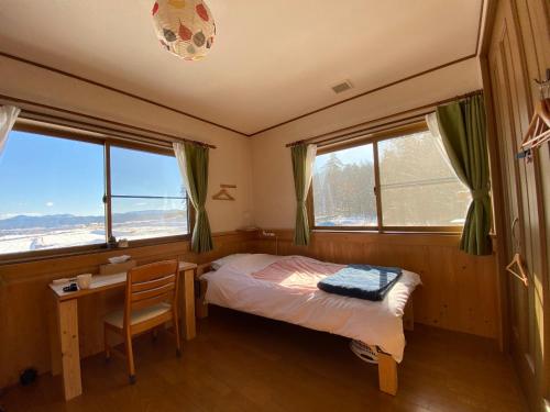 a bedroom with a bed and a desk and windows at Azumino Backpackers in Matsukawa