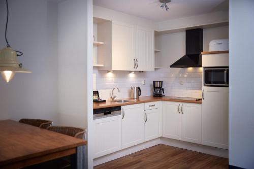 a white kitchen with white cabinets and a table at WestCord ApartHotel Boschrijck in West-Terschelling