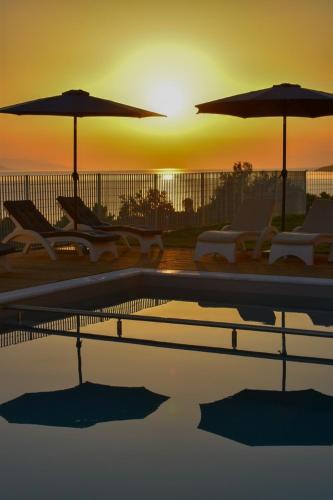 a pool with chairs and umbrellas in front of the sunset at Pantheon Hotel & Suites in Nerotriviá