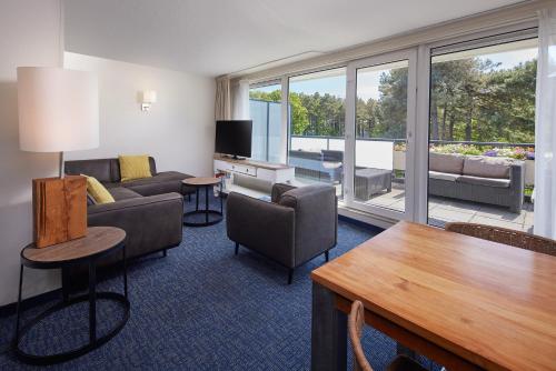 a living room with furniture and a large window at WestCord ApartHotel Boschrijck in West-Terschelling