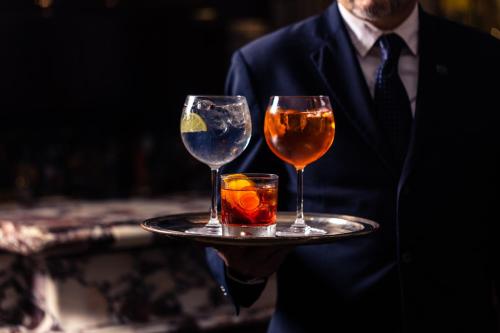 a man in a suit holding a tray with two wine glasses at Hotel Lord Byron - Small Luxury Hotels of the World in Rome