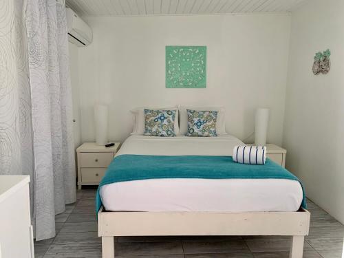 a white bedroom with a white bed with blue sheets at Tu Casita en Aruba in Palm-Eagle Beach