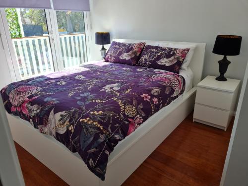 a bed with a purple comforter and a window at Alkion Villa in Wagga Wagga