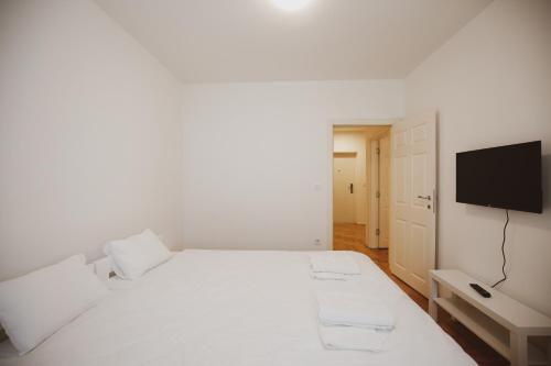 a white bedroom with a white bed and a flat screen tv at Apartman 4, Sinđelićeva 40 in Gornji Milanovac