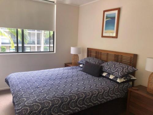 a bedroom with a bed with a blue comforter and a window at Baden 84 Rainbow Shores Walk To Beach Resort Unit Pools Tennis Court in Rainbow Beach