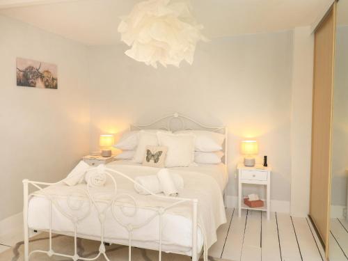 a white bedroom with a white bed and a chandelier at Hope Cottage in Buckfastleigh