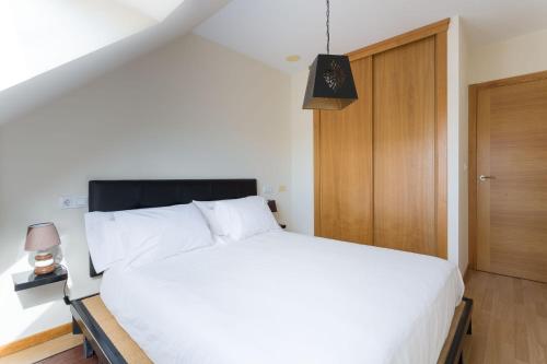 a bedroom with a white bed and a wooden door at ATICO CON TERRAZA A PIE DE PLAYA in Malpica