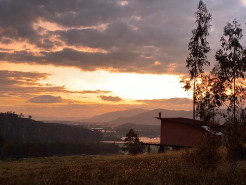 a sunset over a field with a building in the foreground at La Casa de las Estrellas in Suesca