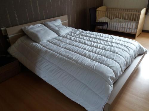 - un grand lit blanc avec des draps blancs et un lit bébé dans l'établissement Appartement meublé agréable au cœur du massif du Jura, à Malpas