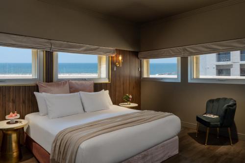 a bedroom with a bed and a chair and windows at Leonardo Gordon Beach in Tel Aviv