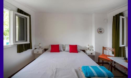a white bedroom with a large bed with red pillows at Anni's cozy apartments 50m from the beach in Agia Triada