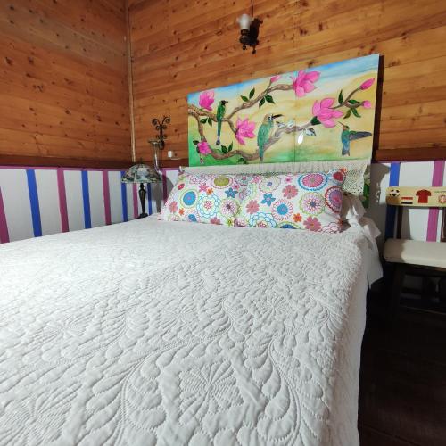 a bedroom with a white bed with a painting on the wall at Hotel Tibouchina in Filandia