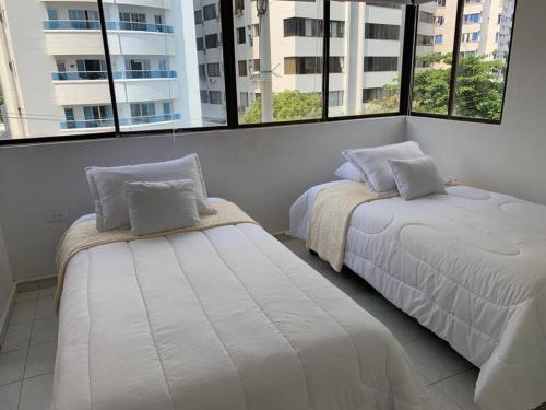 two beds in a room with large windows at Apartamento en el Laguito - Cartagena cerca al mar in Cartagena de Indias