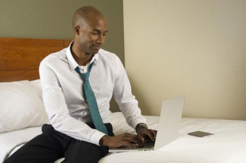 a man sitting on a bed using a laptop computer at WoodSpring Suites Abilene in Abilene