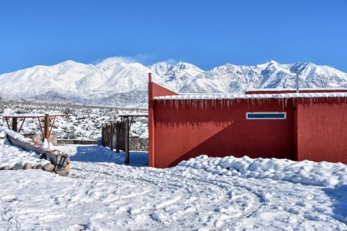 a red building in the snow with mountains in the background at Potre casas de montaña in Potrerillos