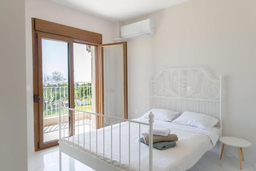 a white bedroom with a bed and a balcony at Vacation house with a panoramic sea view and forest in Polychrono