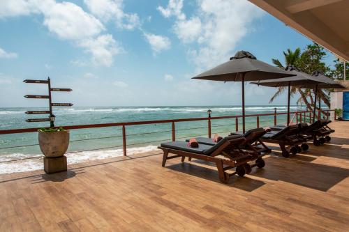 two lounge chairs and umbrellas on a deck overlooking the ocean at Coral Rock by Bansei in Hikkaduwa