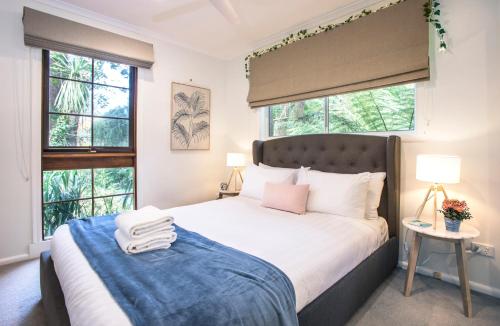 a bedroom with a large bed with two windows at Cosy, central Olinda Camellia Cottage in Olinda