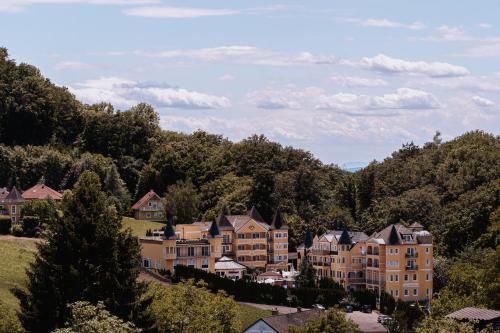 a group of houses on a hill with trees at Schlössl Hotel Kindl in Bad Gleichenberg