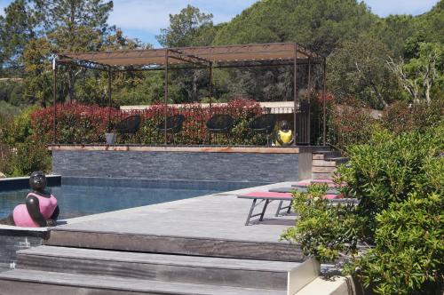 une femme assise à côté d'une piscine avec un kiosque dans l'établissement Les Jardins De Santa Giulia - Charmante chambre dhte, à Porto-Vecchio