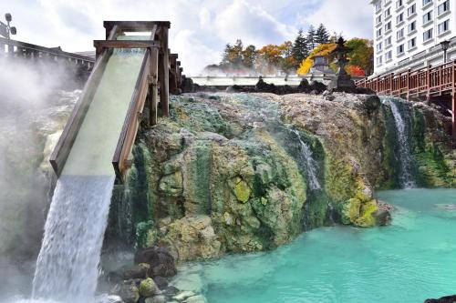 a waterfall on the side of a mountain with a bridge at Urakusatsu TOU in Kusatsu