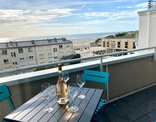 une table avec une bouteille et deux verres sur un balcon dans l'établissement Appartement de standing VUE MER, à Berck-sur-Mer