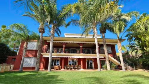 uma casa vermelha com palmeiras em frente em 10 Bedroom 5 Star Luxury Villa & Heated Pool for 5 to 30 Guests near Alicante em Mutxamel