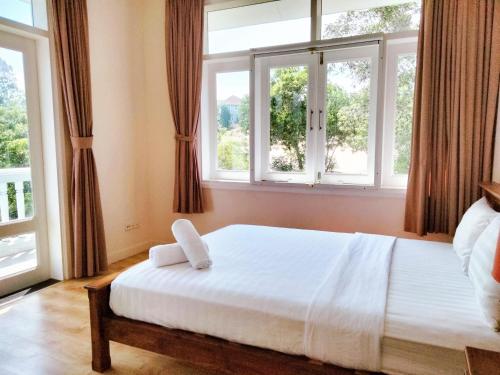 a bedroom with a white bed and two windows at Bougain Villa - Sealinks Mũi Né - chuỗi biệt thự liền kề in Phan Thiet