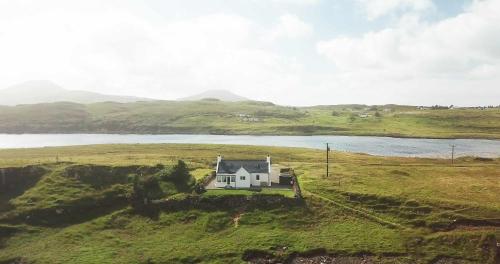 a house on a hill in a field with a body of water at Tigh Beag Na Mara in Roag
