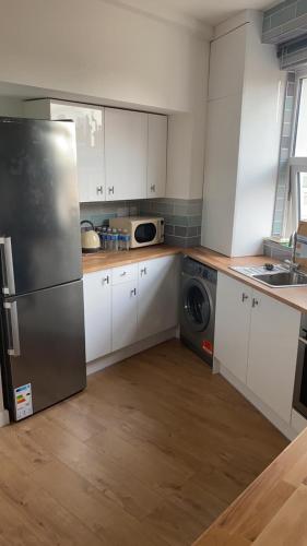 una cucina con armadi bianchi e frigorifero in acciaio inossidabile di Newly refurbished flat in camberwell, london a Londra