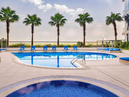 a large swimming pool with palm trees and blue chairs at Adagio Premium Dubai Al Barsha in Dubai