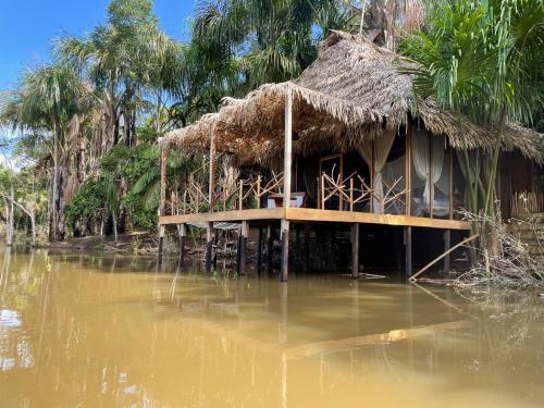 una casa con techo de paja en un cuerpo de agua en Camu camu jungle villa on Aguajale lake - supboard&vinyl, en Iquitos