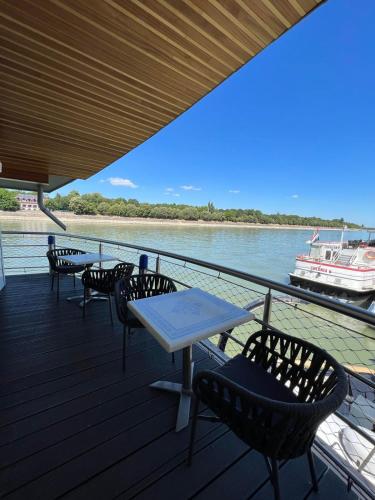 a deck with tables and chairs and a boat on the water at Vogue Boat Apartments in Budapest