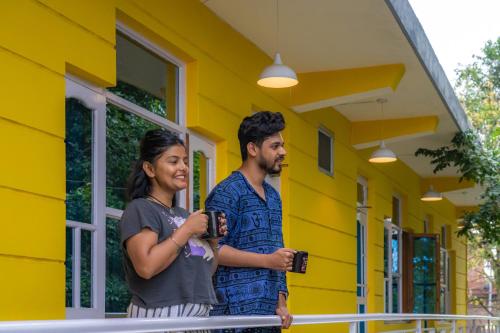 a man and a woman standing outside of a yellow house at Whoopers Hostel Bir in Bīr