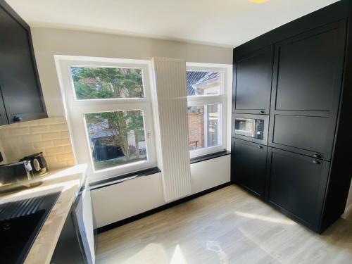 a kitchen with black cabinets and two windows at Lovely, renovated appartment, near the beach. in De Haan
