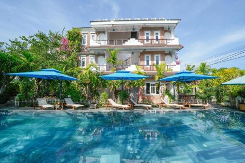 a hotel with a large swimming pool with blue umbrellas at Blooms Boutique Village in Hoi An