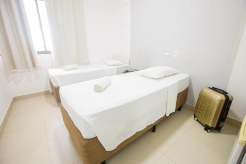 2 camas en una habitación blanca con una maleta en Rede Andrade Ondina Salvador, en Salvador