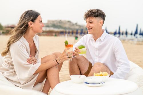 a man and woman sitting on the beach with drinks at Pizzomunno Vieste Palace Hotel in Vieste