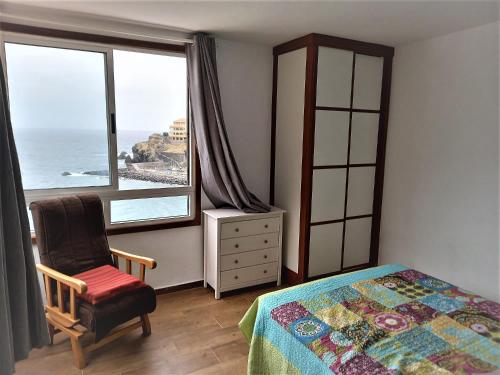 um quarto com uma cama, uma cadeira e uma janela em Jema Apartamento Playa San Marcos by HRTenerife Net em Icod de los Vinos