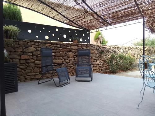 a patio with three chairs and a stone wall at Gite d'Emma in Camaret-sur-Aigues
