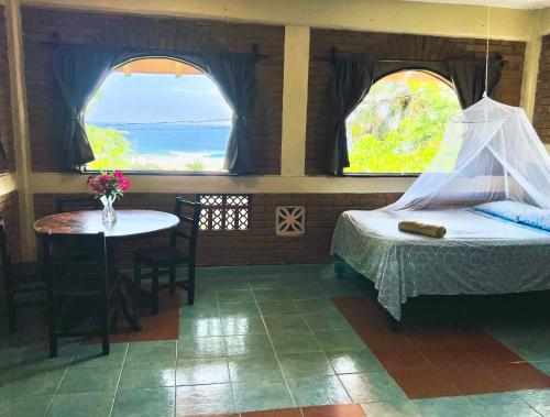 a bedroom with a bed and a table and two windows at Ananda Guest House Yoga & Meditación in Puerto Escondido