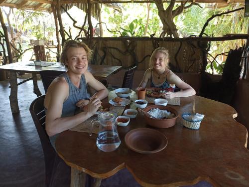 dos personas sentadas en una mesa de madera comiendo comida en Nature Beach Huts, en Trincomalee