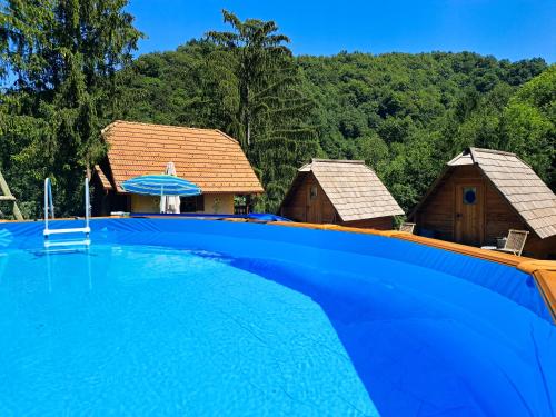 a large blue swimming pool with two cottages at Glamping Zeleni turizem in Makole