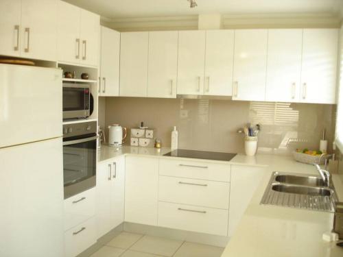 a white kitchen with white cabinets and a sink at Cosy Cottage near the beach in Booker Bay