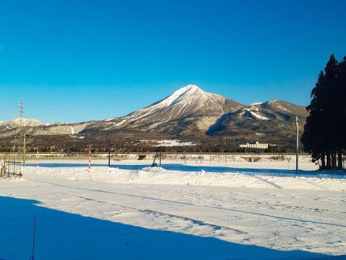 a snow covered field with a mountain in the background at Guest House Inawashiro~Hanbog~ in Inawashiro