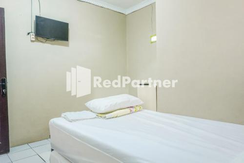 a room with a bed with white sheets and a television at Penginapan Rio Anakku Syariah Banjaran Mitra RedDoorz in Pameungpeuk