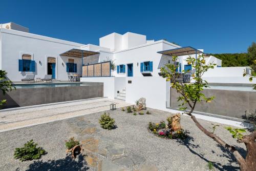 une maison blanche avec un arbre dans la cour dans l'établissement Kalathos Square luxury suites, à Kalathos