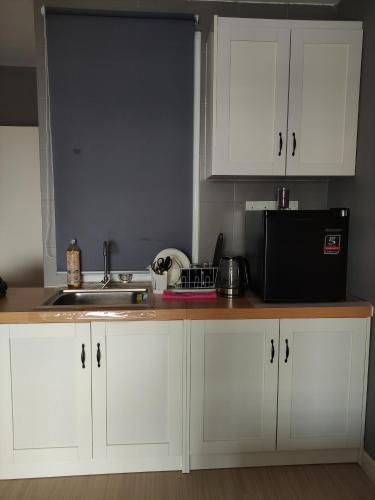 a kitchen with white cabinets and a sink and a microwave at Kampar Bonvoy Champs Elysees 4pax Homestay in Kampar